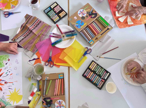 Kreatives Arbeiten beim Kurs „Die Kunst des Alterns“. Fotoaufnahme von Petra Siebenhaar. Die Abbildung zeigt einen bunt mit diversen Kreativmaterialien gedeckten Tisch. Die älteren Teilnehmenden des Kurses gestalten damit ihre eigenen Kunstwerke. Die Fotoaufnahme stammt von Petra Siebenhaar.